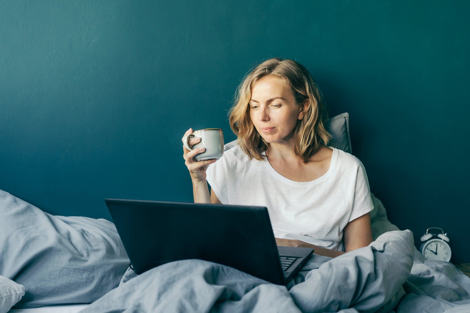A woman is sitting in bed and typing on a laptop.