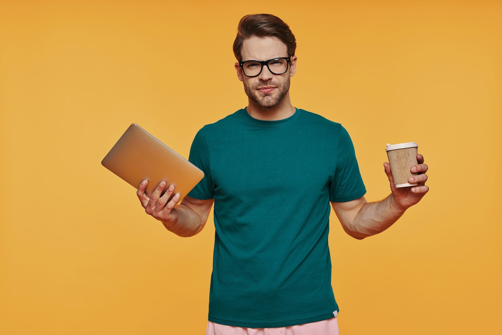 Handsome young man in casual clothing carrying digital tablet and cup